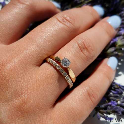 Delikatna, damska obrączka z brylantami zaprezentowana na dłoni z klasycznym pierścionkiem zaręczynowym